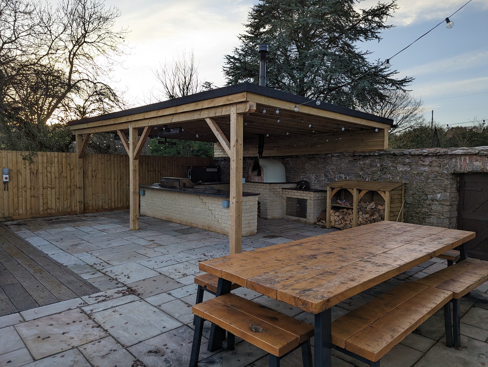A timber garden shelter with a flat felt roof over a paved patio